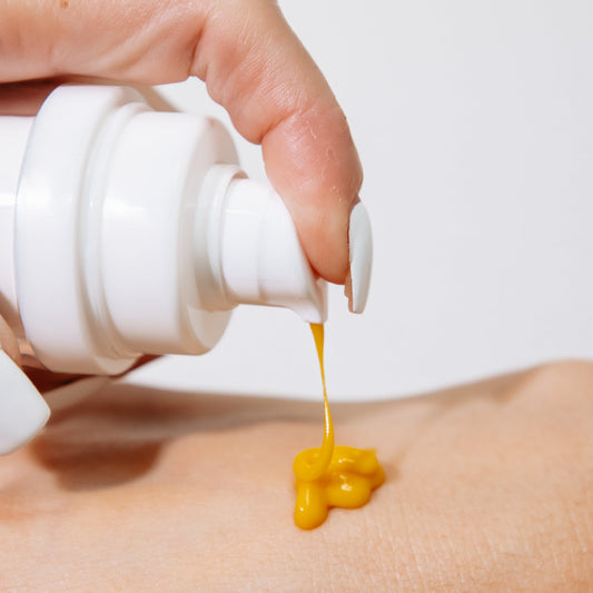 Hand applying Truology A2 yellow cream from a white bottle onto skin